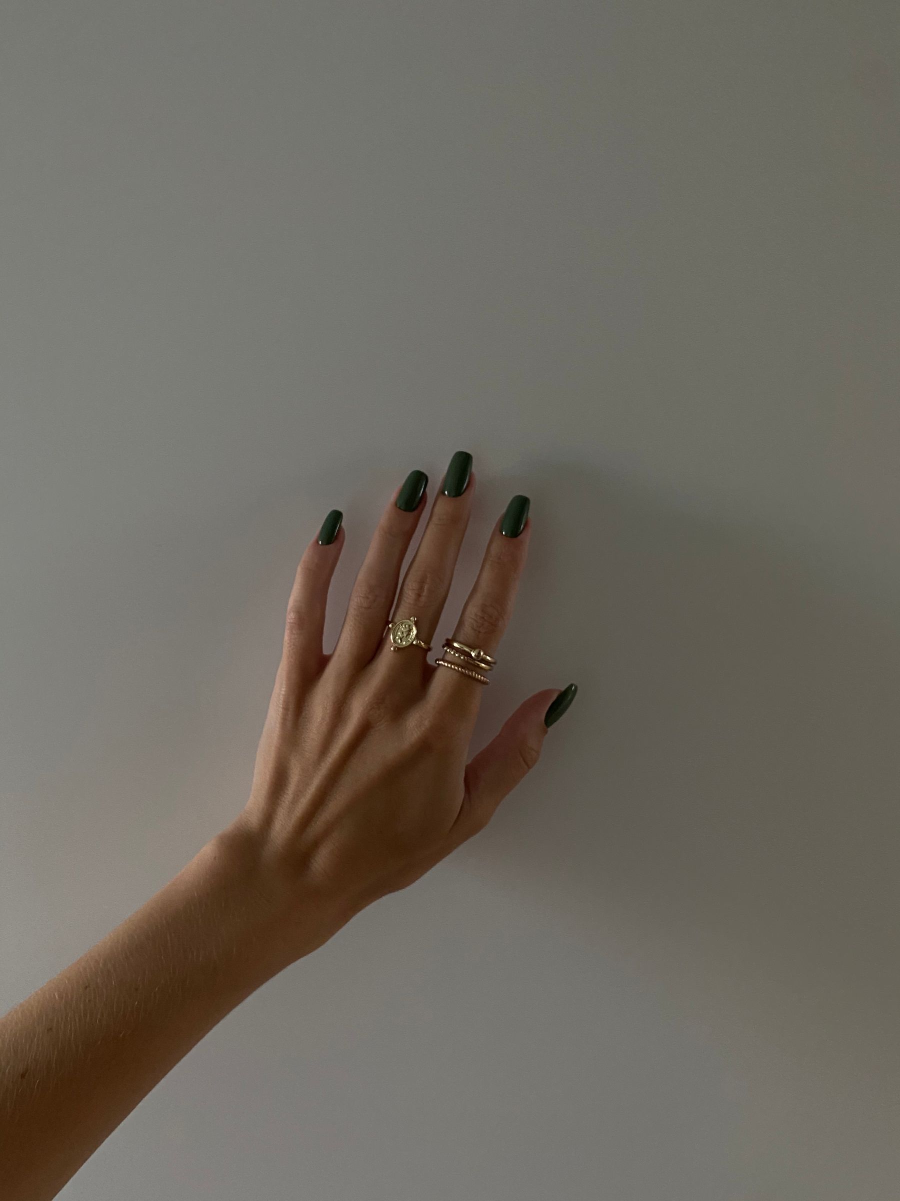 Hand with dark green nail polish and rings