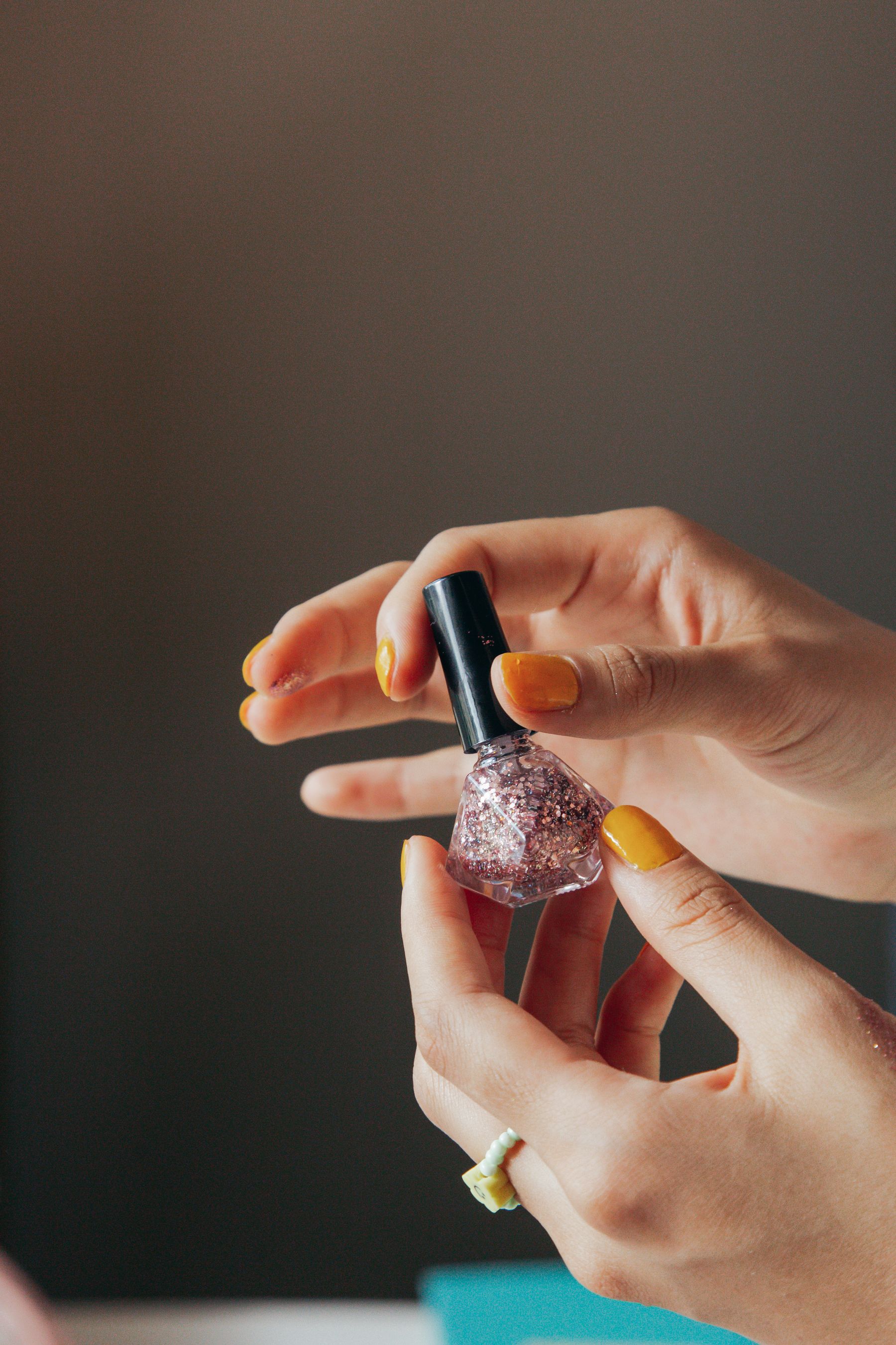 Manicured hands holding a glitter nail polish bottle